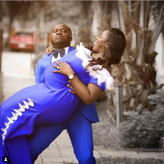 Man struggles to carry his pregnant wife in maternity photo shoot.