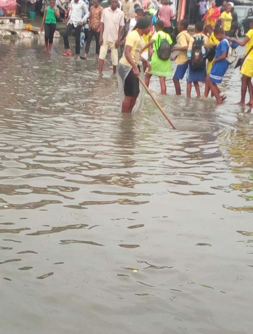 Nigerian Lady Goes Under The Rain To Help School Children Cross A Flooded Market