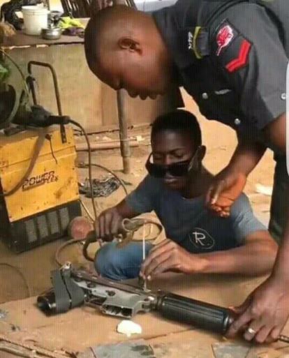 Checkout This Viral Photo Of A Nigerian Policeman Fixing His Gun At A Roadside Welder's Shop.